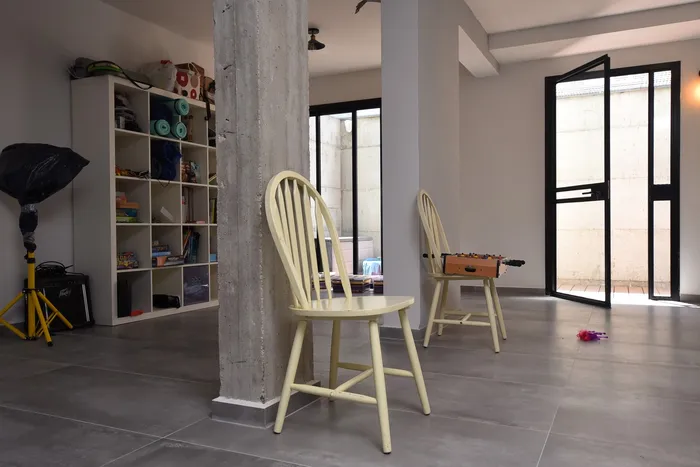 מרתף מואר עם עמוד בטון חשוף, כיסאות עץ ודלתות ברזל