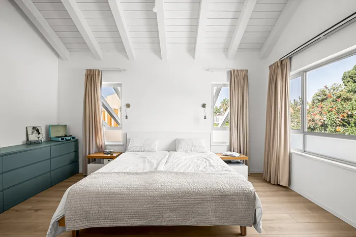 חדר שינה עם תקרת קורות, וילונות פשתן ושידת טיל