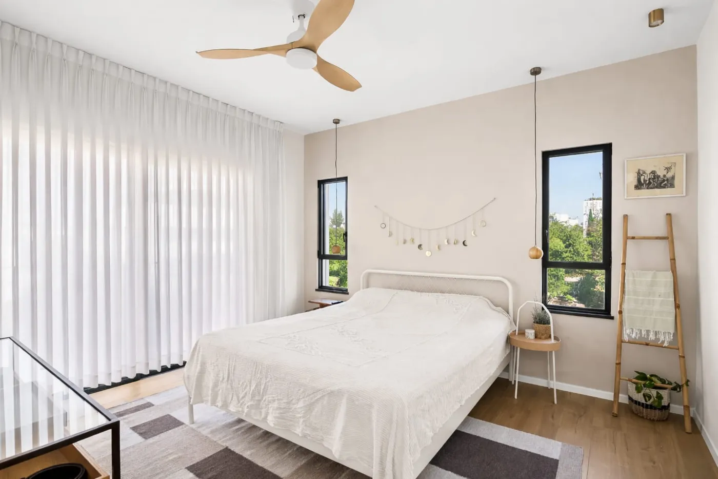 חדר שינה עם קיר בגוון בז׳, ריצוף אלון ומאוורר תקרה מעץ