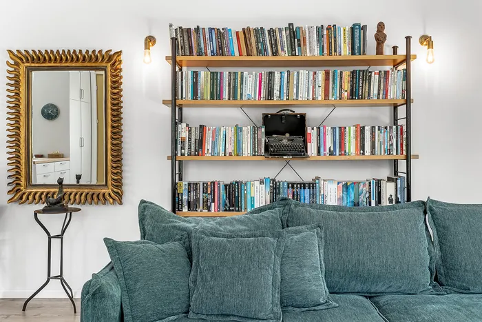 ספה ירוקה עם ספריית אלון, מכונת כתיבה ומראה זהב