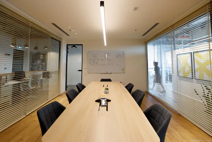 חדר ישיבות עם שולחן עץ ארוך, תאורה לינארית ומחיצות זכוכית