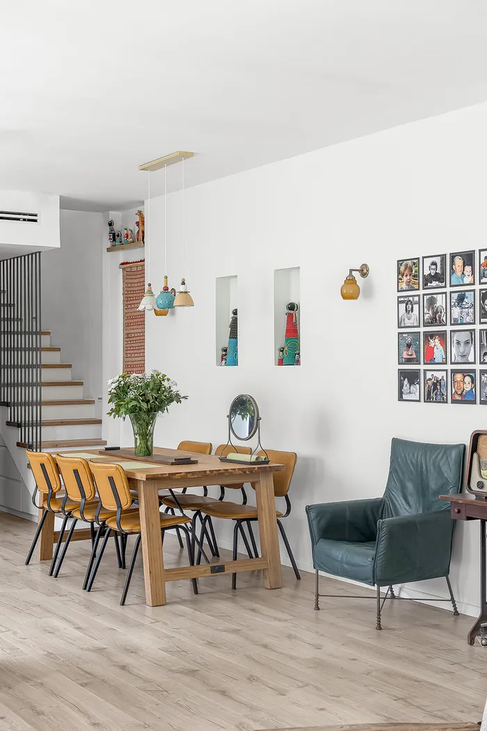 פינת אוכל עם כסאות צהובים, גופי תאורה, כורסת עור ירוקה וקיר תמונות