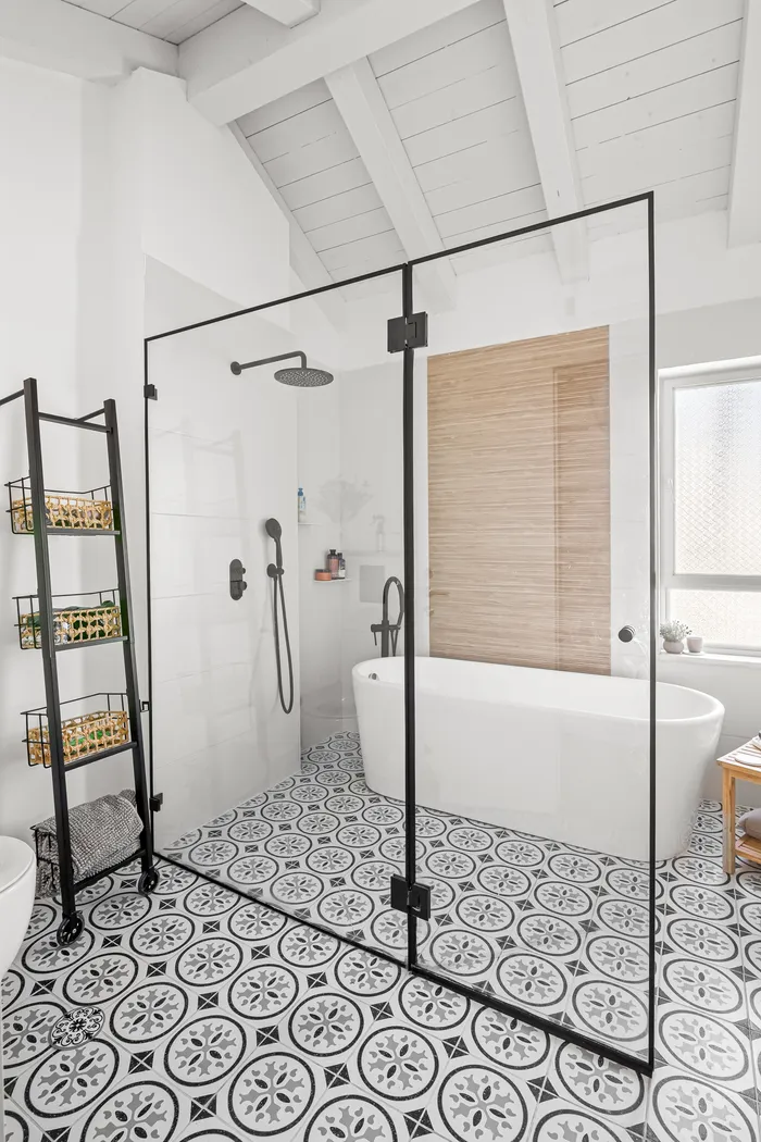 חדר רחצה עם אריחים מעוטרים, מקלחון זכוכית ואמבט חופשי תחת תקרת קורות