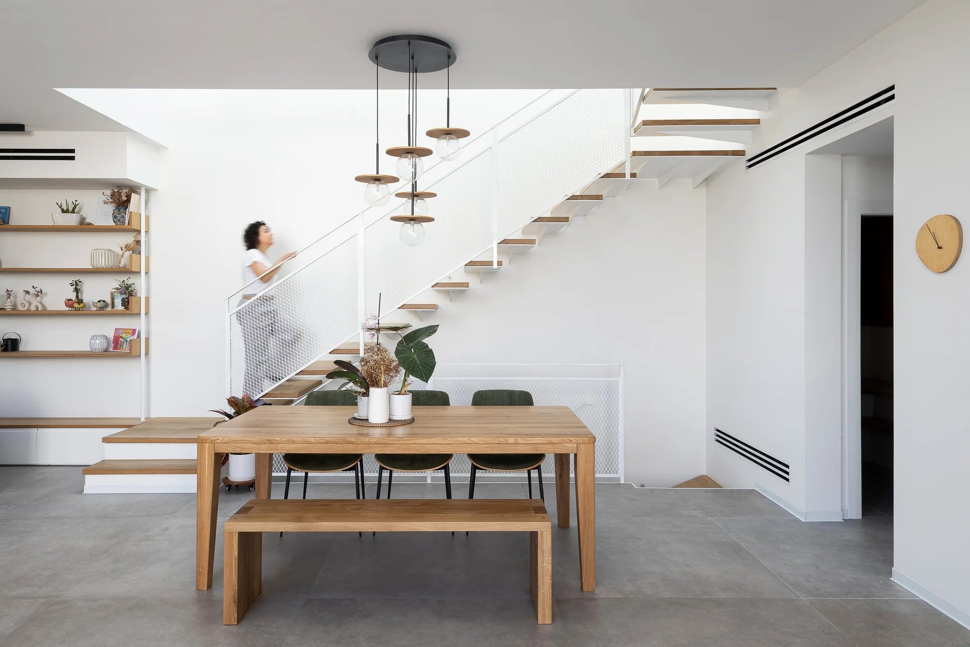 חלל מגורים פתוח עם שולחן אלון, גרם מדרגות מרחף ותאורת תקרה