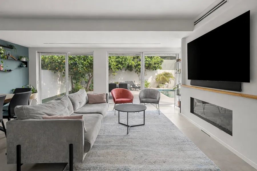 סלון עם קמין, ספה אפורה ונוף לבריכה דרך דלתות זכוכית