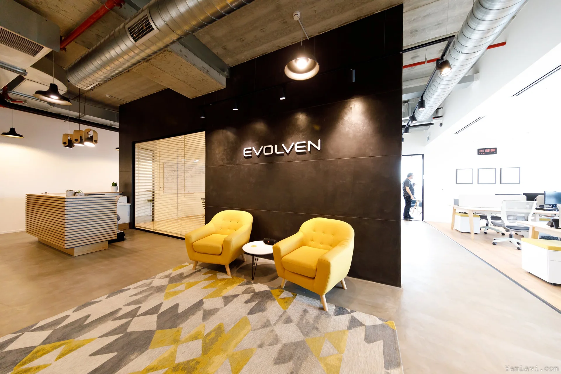 המשרדים בגבעת שמואל — לובי קבלה עם קיר ממותג כהה, כורסאות צהובות ותקרה תעשייתית