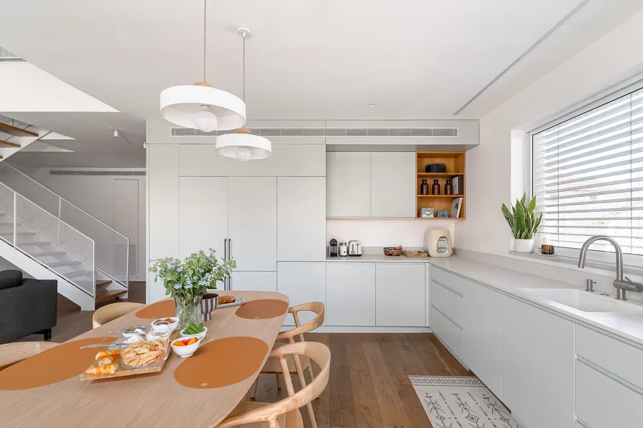 מטבח בהיר עם ארונות מנטה, נישת אלון ומדרגות ברקע