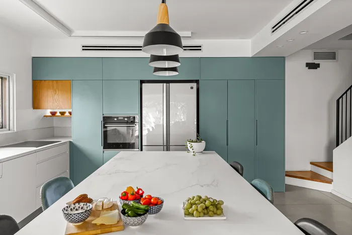 מטבח עם אי שיש לבן, ארונות טורקיז וגופי תאורה שחורים