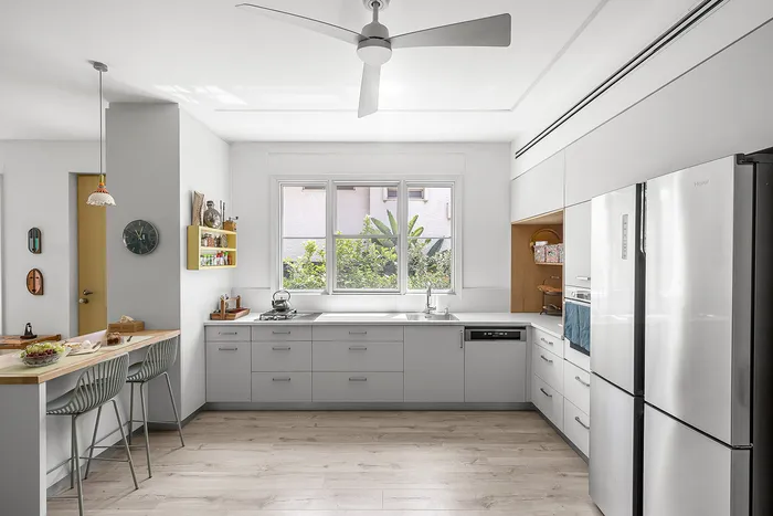 מטבח בהיר עם ארונות אפורים, מאוורר תקרה וחלון לגינה