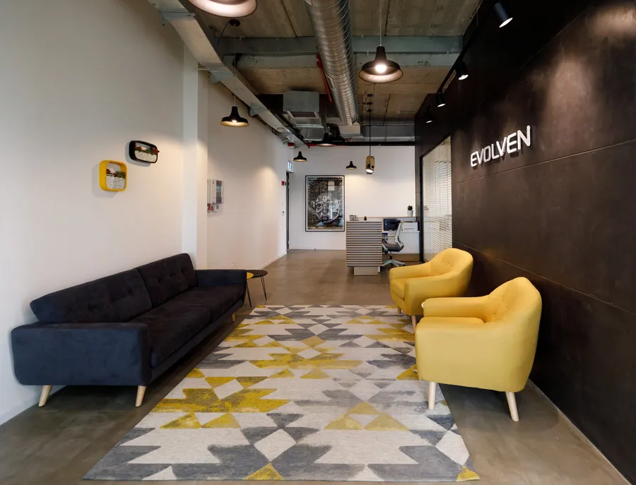 לובי עם ספה כהה, כורסאות צהובות ושטיח גיאומטרי על רקע קיר ממותג