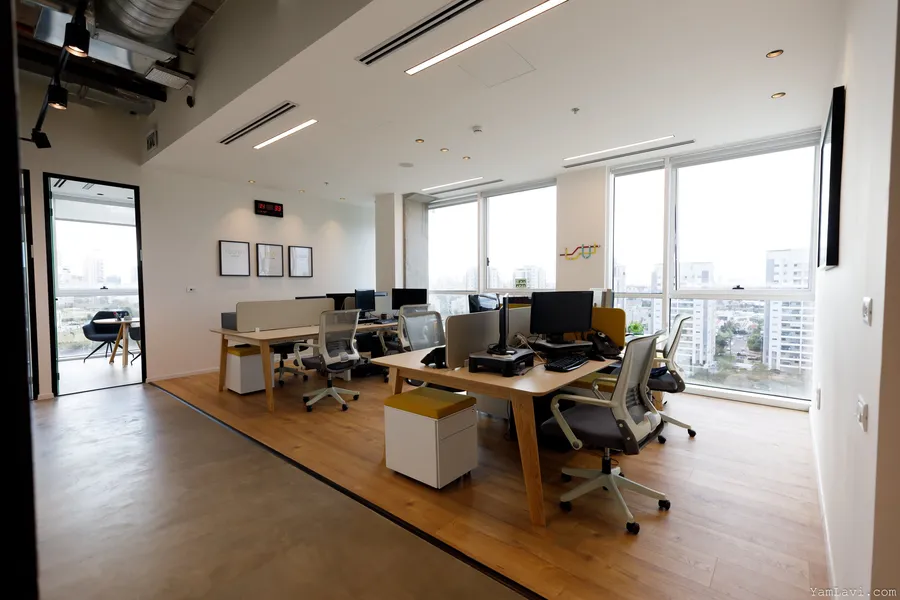 חלל עבודה פתוח עם שולחנות עץ, חלונות פנורמיים ונוף עירוני