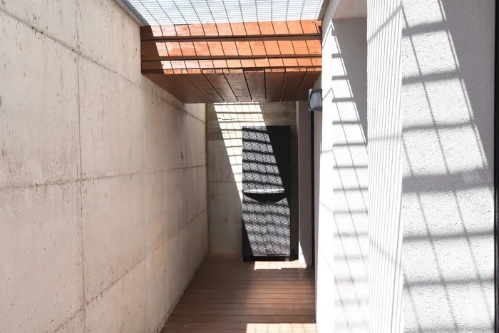 מעבר חיצוני עם קירות בטון חשוף, דק עץ ופרגולה