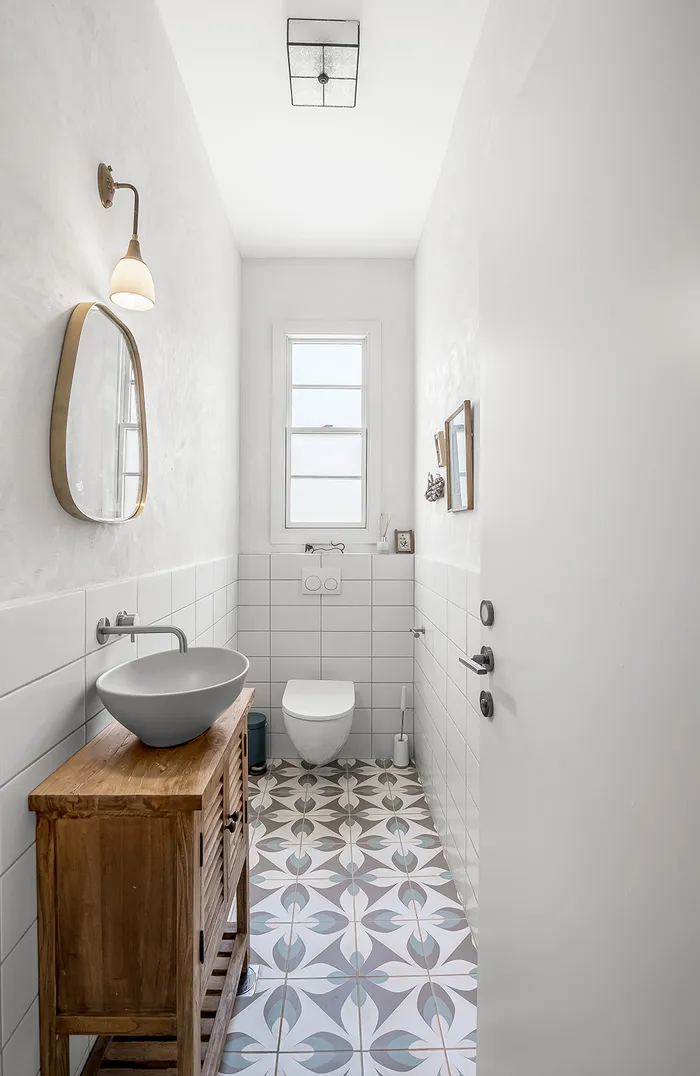 חדר שירותים צר עם ריצוף מעוטר, ארון עץ וכיור קערה