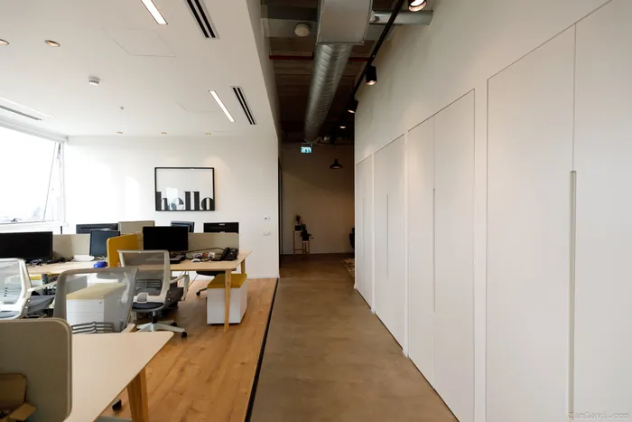 מסדרון עבודה עם ארונות לבנים, תקרה חשופה ותאורה תעשייתית